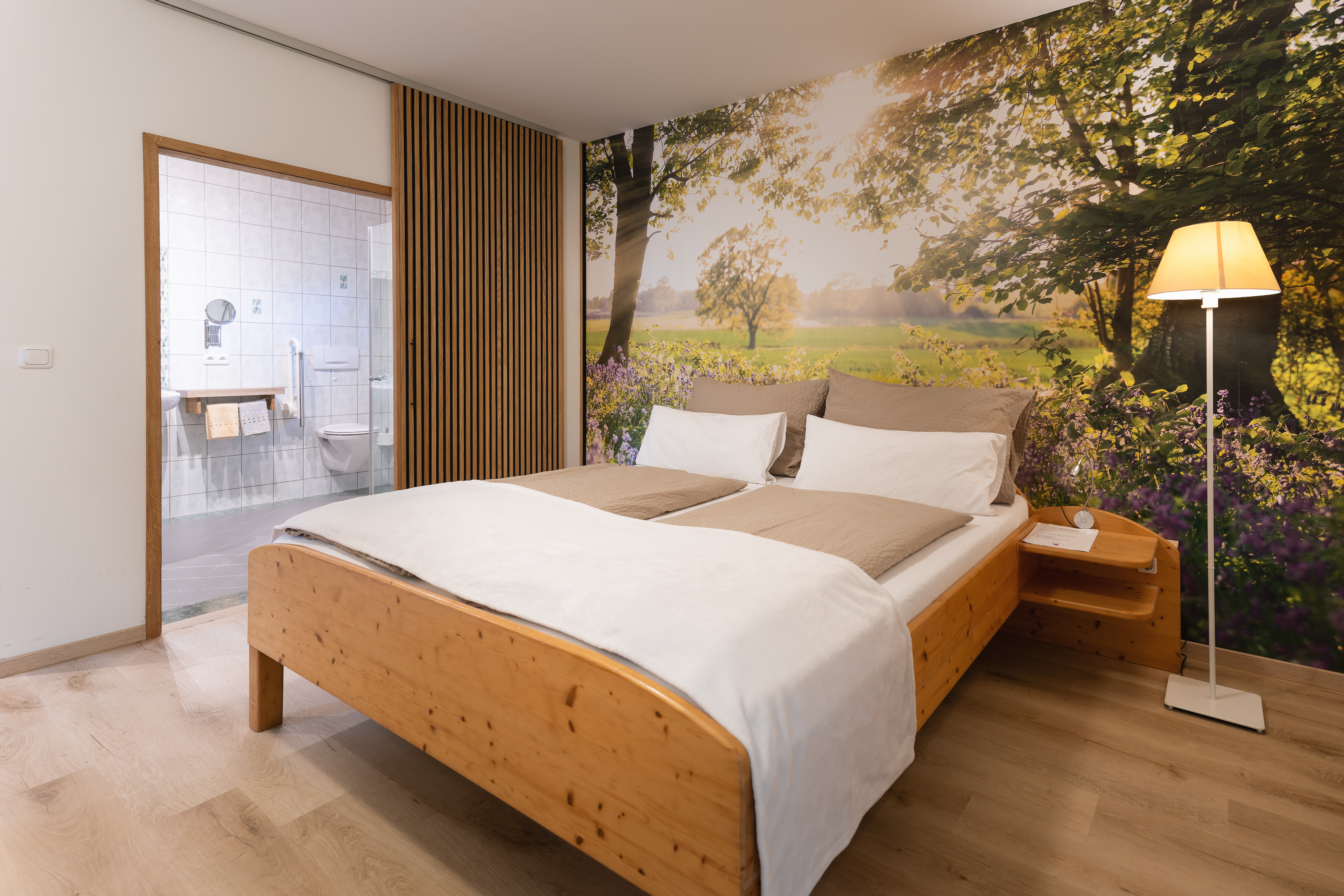 Bauernhofurlaub-Angebot: Schlafzimmer mit Doppelbett aus Naturholz mit schöner Wandtapete und Sonnenaufgang. Blick in das angrenzende Badezimmer - AnRadeln Wochenende in Bad Radkersburg